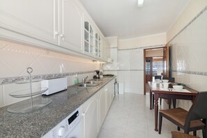 Una cocina con armarios blancos, encimera de granito, lavavajillas y un comedor con mesa y sillas.