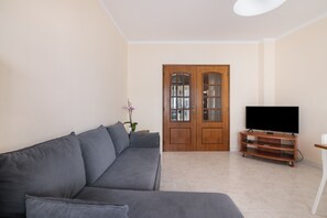 Una sala de estar con un sofá, un televisor sobre un mueble de madera y una puerta con paneles de vidrio.