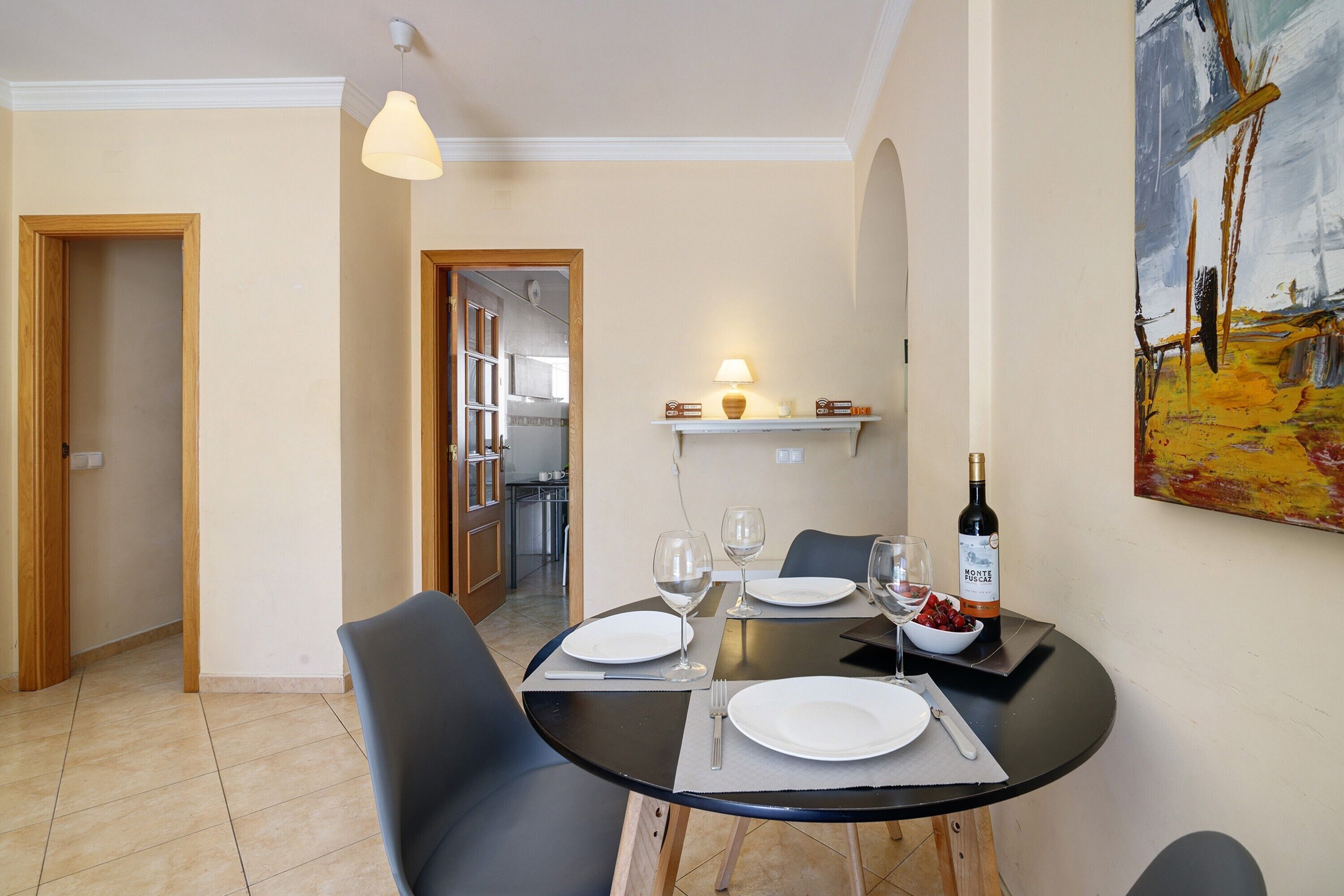 Un coin repas avec une table ronde, des chaises, une bouteille de vin et un tableau accroché au mur.