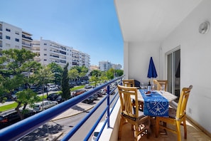Ein Balkon mit Esstisch, der auf eine Straße mit parkenden Autos und Gebäuden blickt.