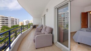 A balcony with a sofa, a bed, and a view of buildings. - Apartment 'Rei  3º T' with Balcony, Wi-Fi and Air Conditioning (Quarteira)