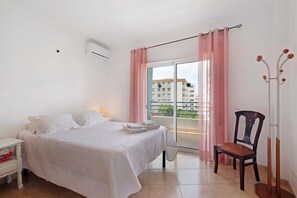 Une chambre à coucher comprenant un lit, une chaise, une table de chevet et un balcon avec vue sur les immeubles.