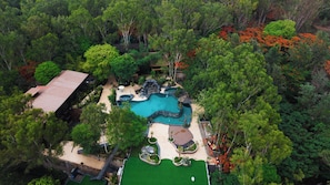 Vista aérea de un resort con piscina, un edificio pequeño y follaje circundante.