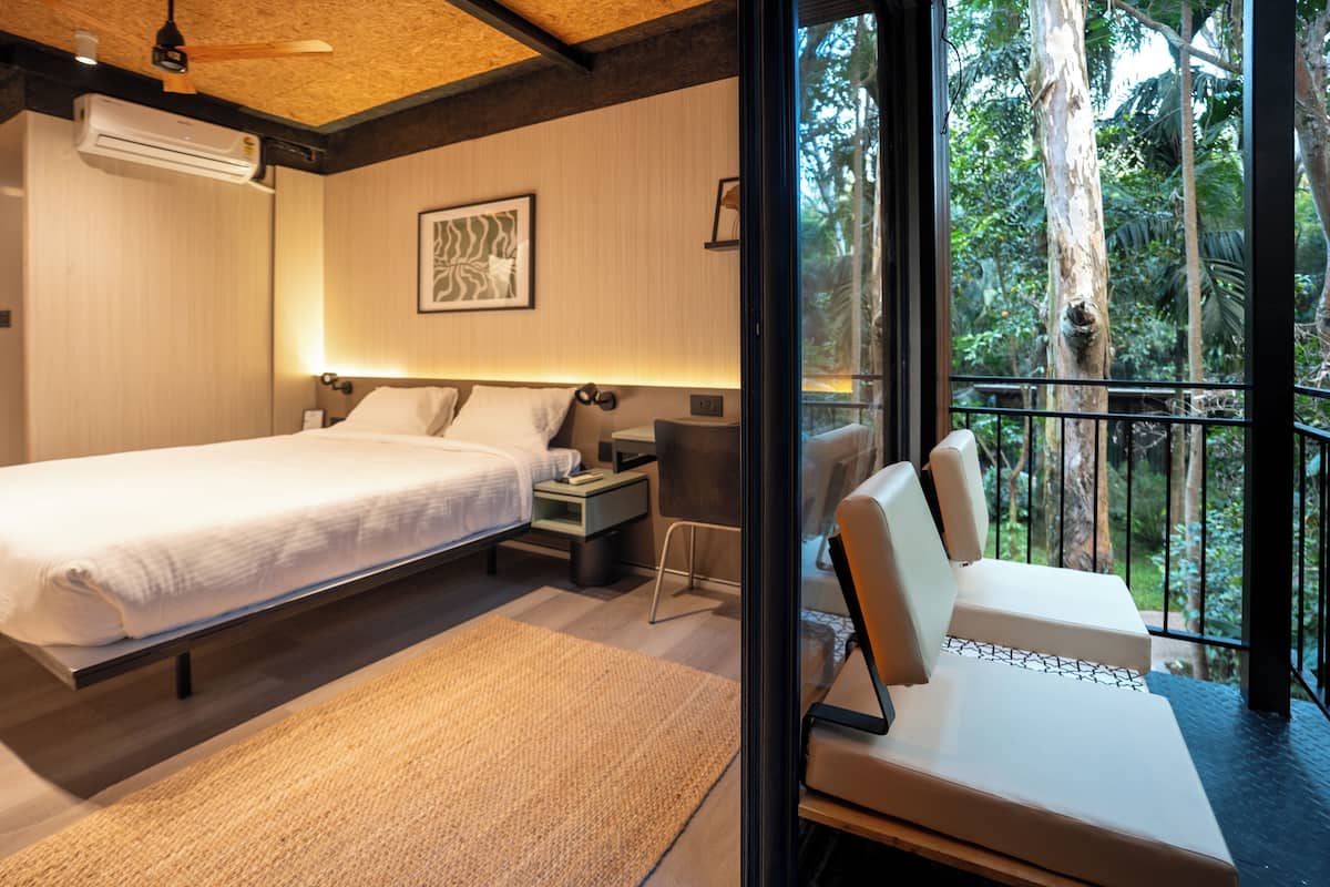 Un dormitorio con cama, mesitas de noche, un escritorio y vistas al exterior.