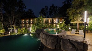 A modern building with a swimming pool, surrounded by lush greenery and a well-lit patio area. - Area 83 Adventure Resort (Anekal)