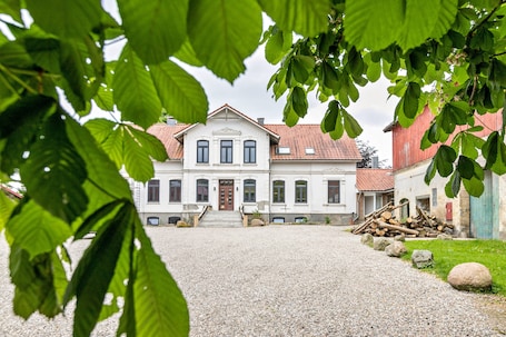 A large building with a symmetrical facade, a gravel driveway, and a pile of logs.. Holiday Apartment on Traditional Three-Sided Farm