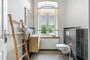 A modern bathroom with a wooden ladder, a window with blinds, a toilet, and a radiator.