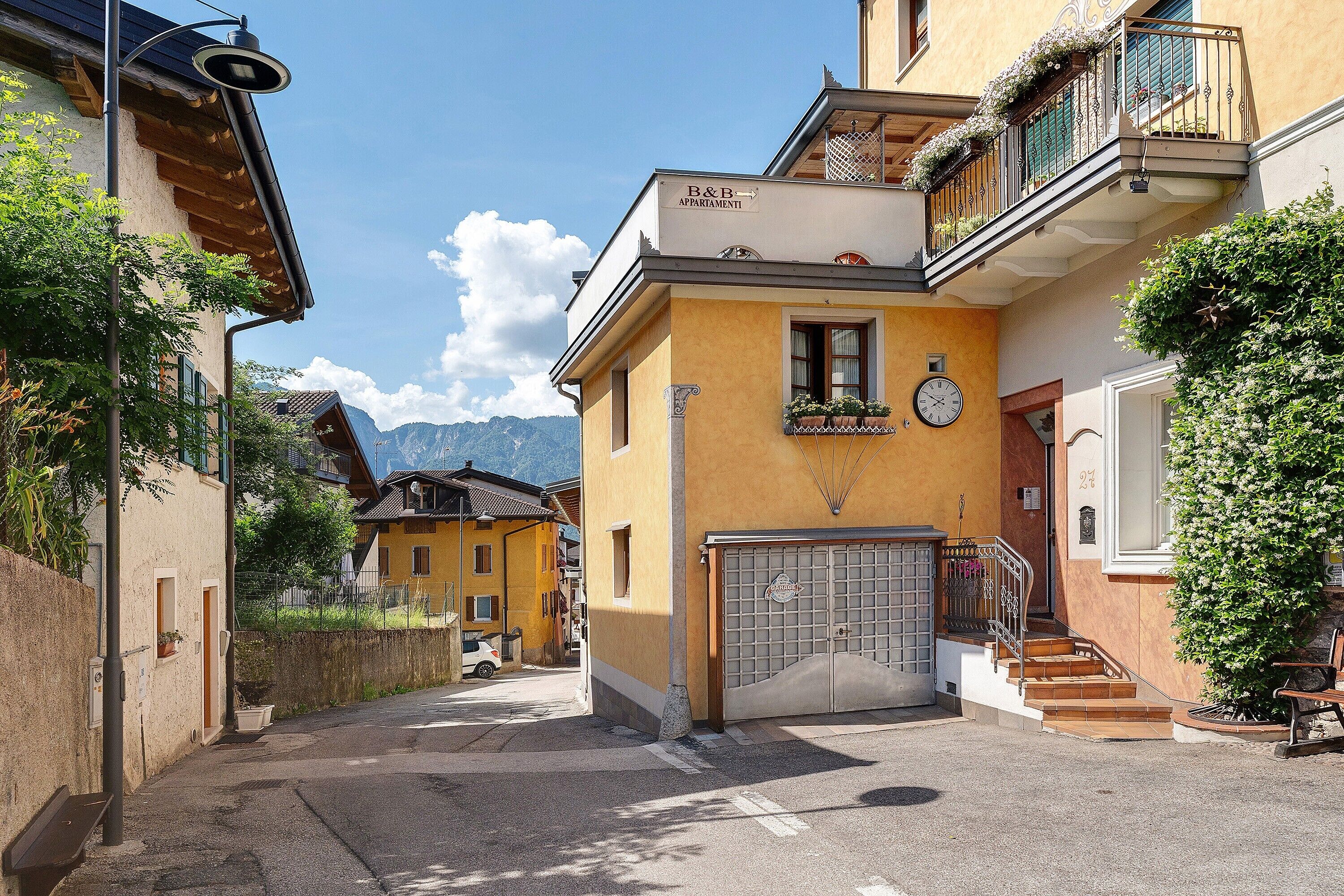 Un vicolo stretto con un edificio giallo, un cancello e una scala che conduce a un balcone con piante.
