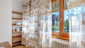 Cozinha com estantes de madeira, janela com cortinas e radiador.