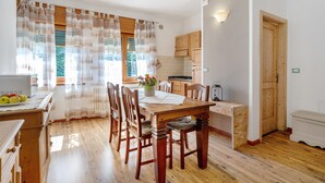 Uma área de refeições com mesa e cadeiras de madeira, uma cozinha com armários de madeira, e uma janela com cortinas.