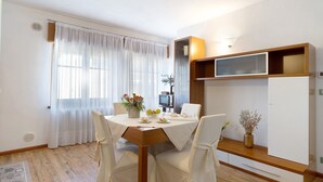 A dining area with a table set for two, a microwave, and a cabinet with a shelf.