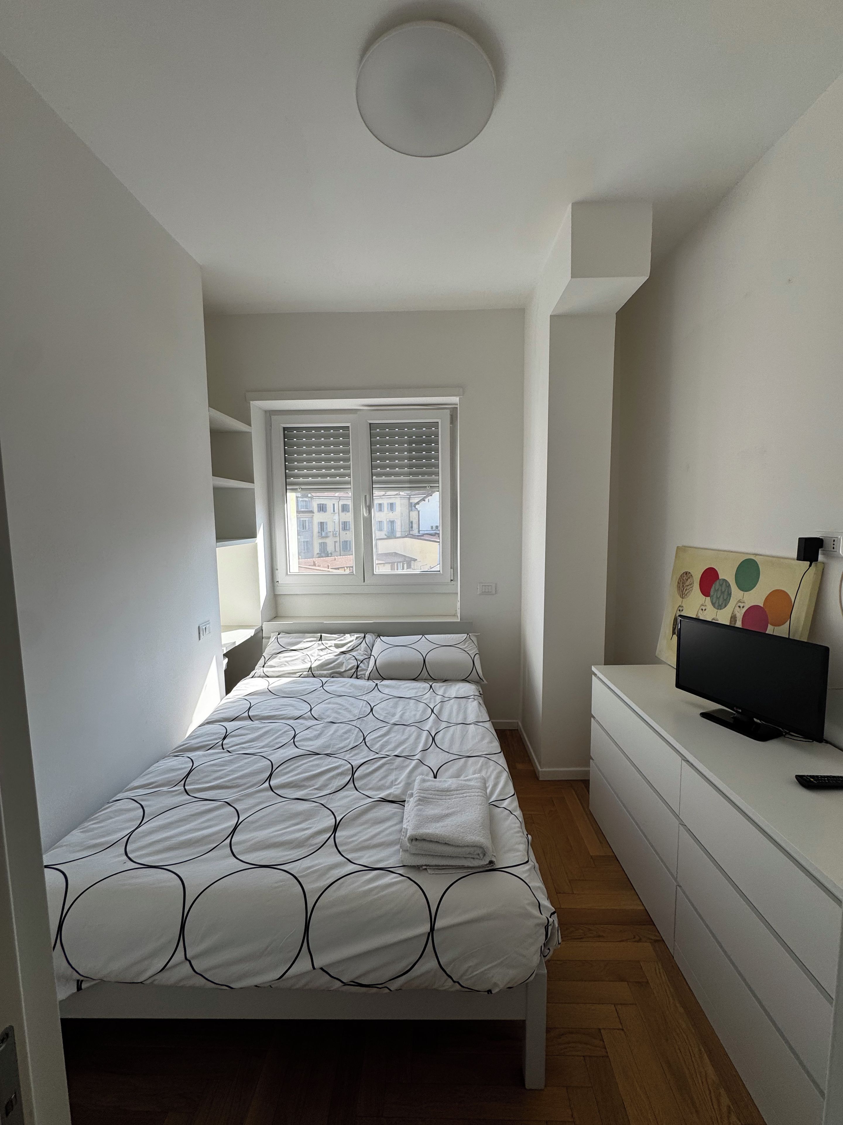 Ein Schlafzimmer mit einem Bett, einem Fernseher, einem Schminktisch und einem Fenster mit Jalousien.
