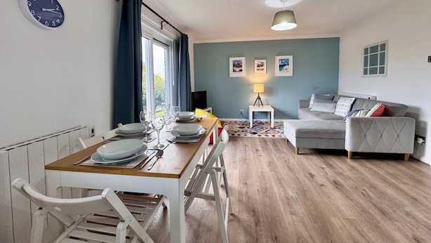 En matplats med ett bord dukat för fyra personer, en soffa, en lampa och inramade tavlor på väggen.