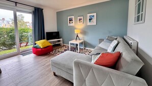 Ett modernt vardagsrum med en soffa, en röd sittpuff, en tv på ett tv-bord, en lampa och inramade tavlor på väggen.