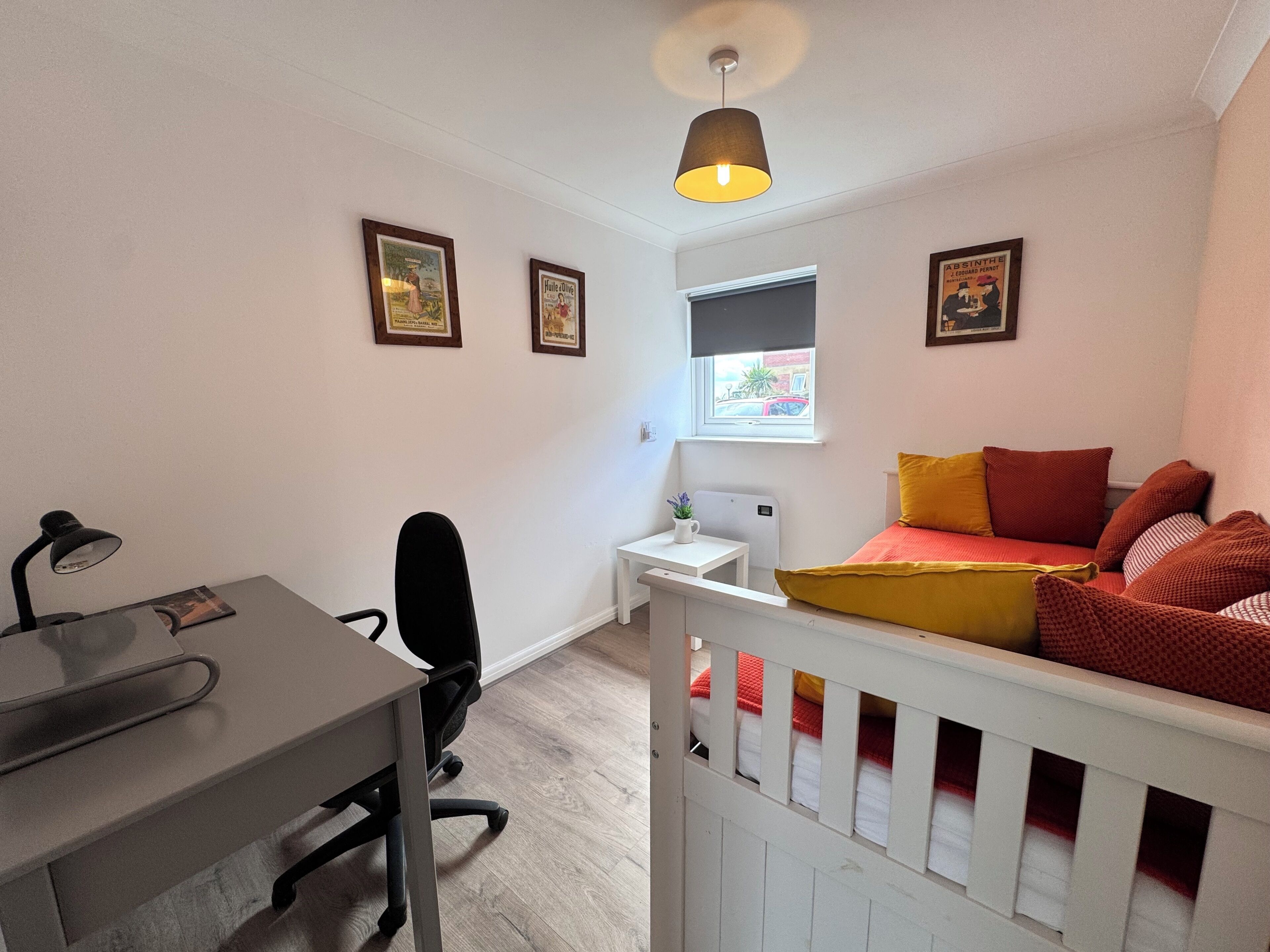 A bedroom with a desk, chair, bed, window, and ceiling light.
