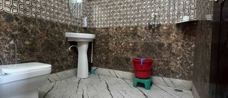A bathroom with a white toilet, a pedestal sink, a red and green bucket, and a patterned wall.
