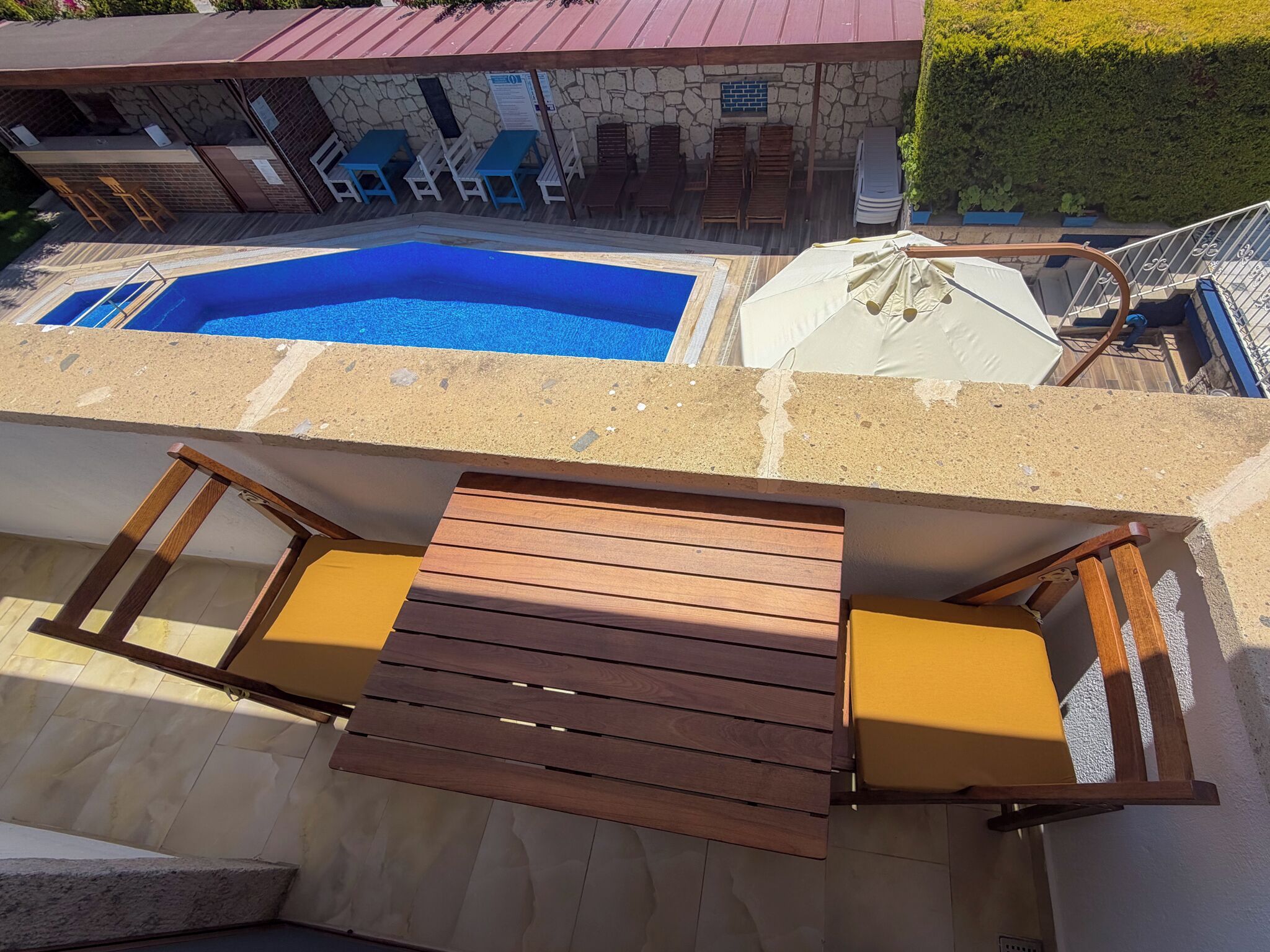 A pool area with a wooden deck, lounge chairs, and a stone building in the background.