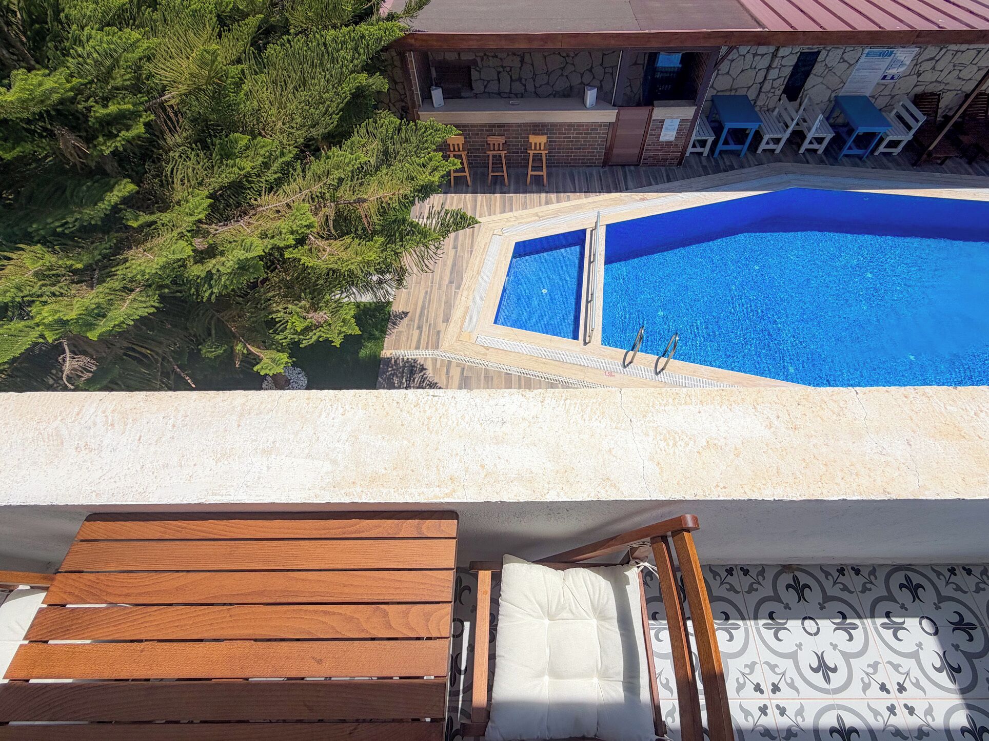 A rooftop pool with a stone wall, wooden deck, and lounge chairs.