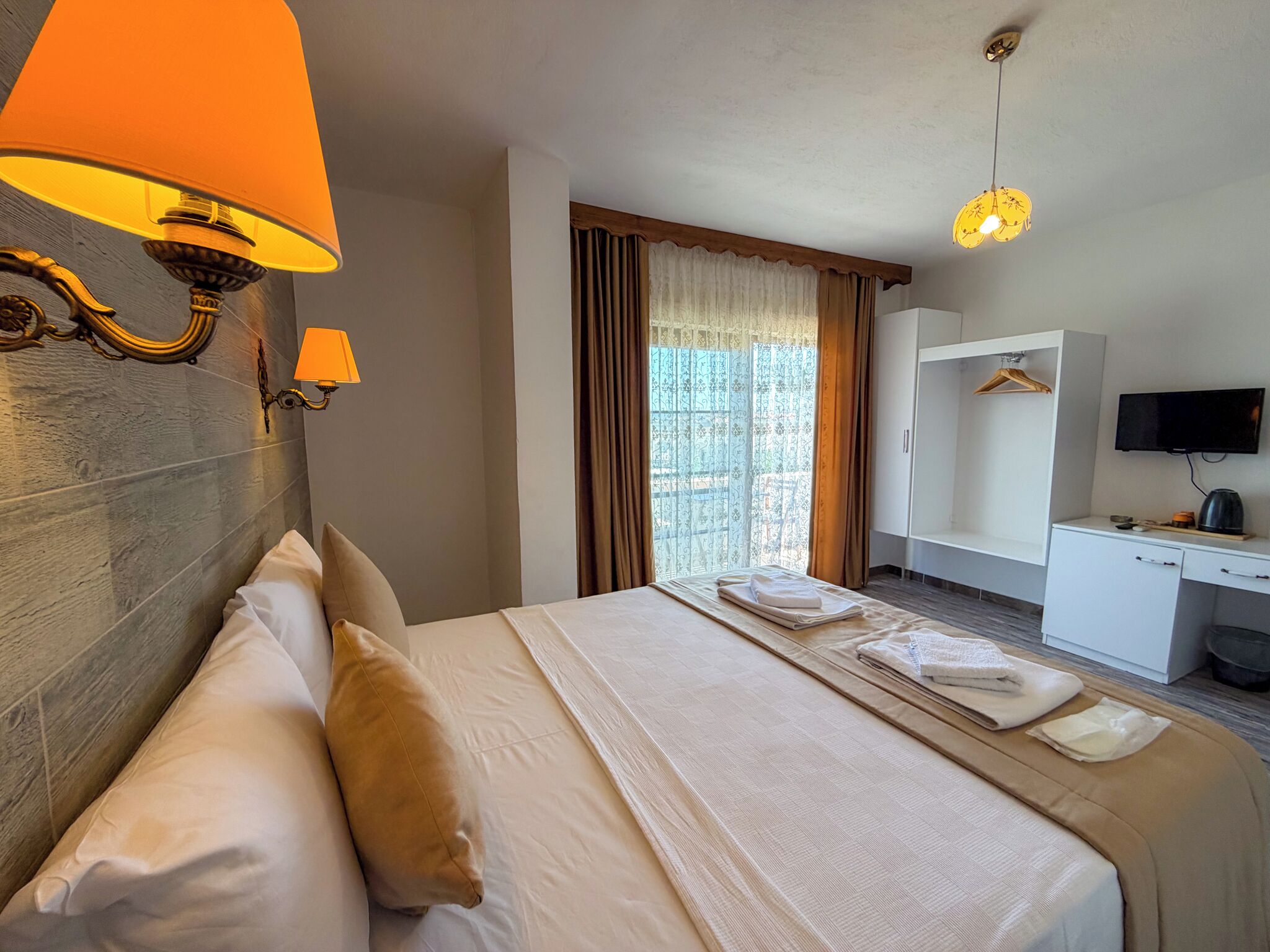 Ein Hotelzimmer mit Bett, Nachttischlampen, Fernseher, Schreibtisch und einem Fenster mit Vorhängen.