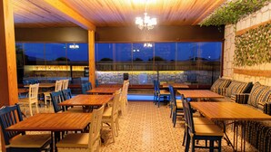 An indoor dining area with wooden tables and chairs, stone walls, and a view through large windows. - Alatrio Hotel Alaçatı (Cesme)