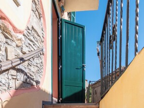 Una calle estrecha con una puerta verde, pared de piedra y barandilla de metal.