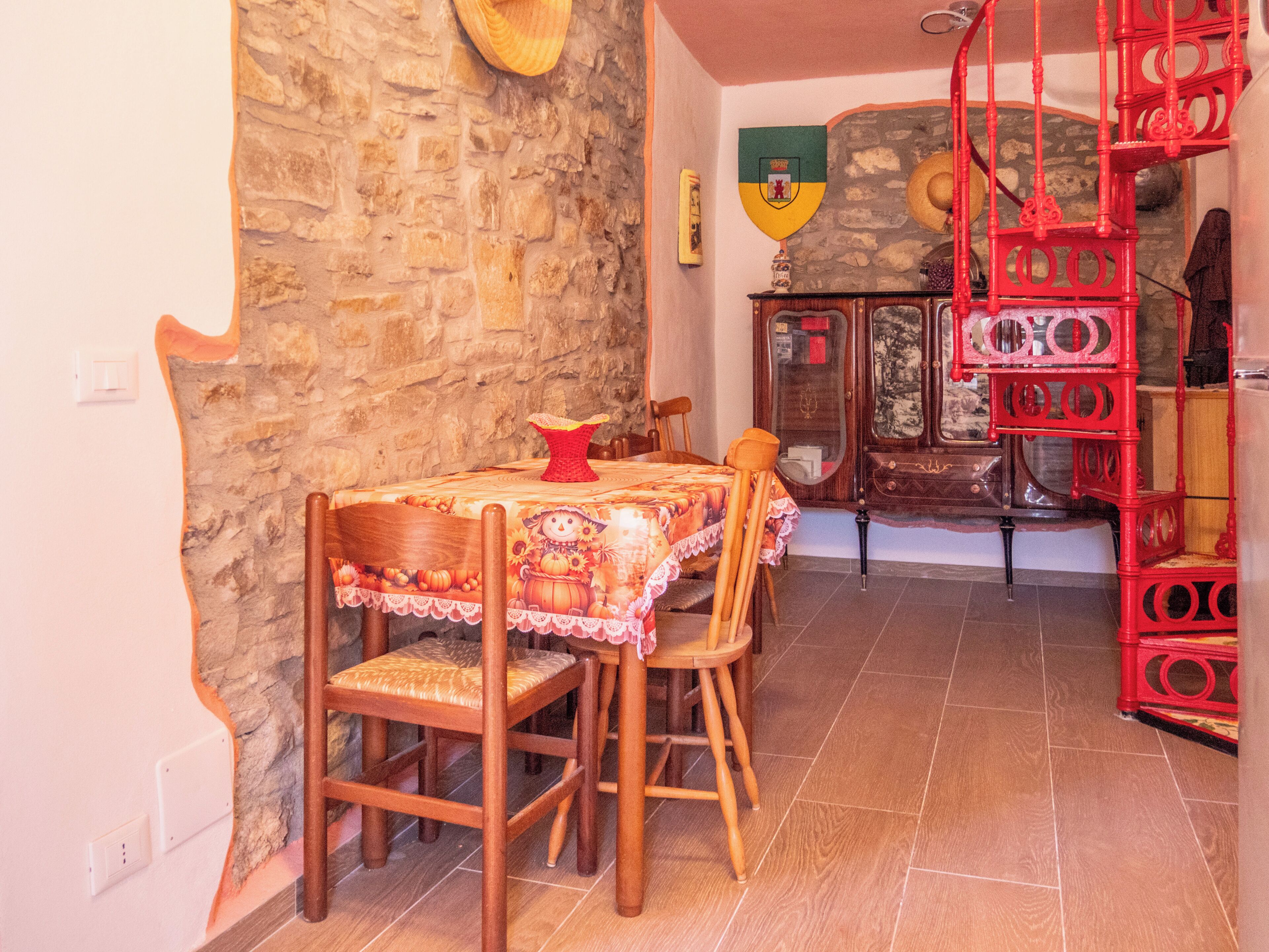 A dining area with a stone wall, wooden chairs, a table with a tablecloth, and a red metal rack.