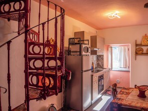 Una cocina con escalera de caracol, un refrigerador, un microondas y un ventanal con cortinas.