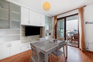 A modern kitchen with a flat-screen TV, white cabinets, and a dining area with a glass table and chairs. - Vivienne In Front Of Pool Holiday Home with Shared Pool, Wi-Fi & Air Conditioning (Desenzano del Garda)