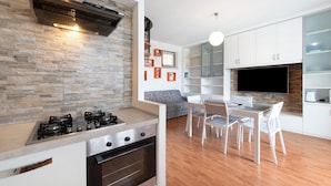 A modern kitchen with a gas stove, oven, and a built-in range hood. There is a dining area with a table and chairs, and a TV mounted on the wall. - Vivienne In Front Of Pool Holiday Home with Shared Pool, Wi-Fi & Air Conditioning (Desenzano del Garda)
