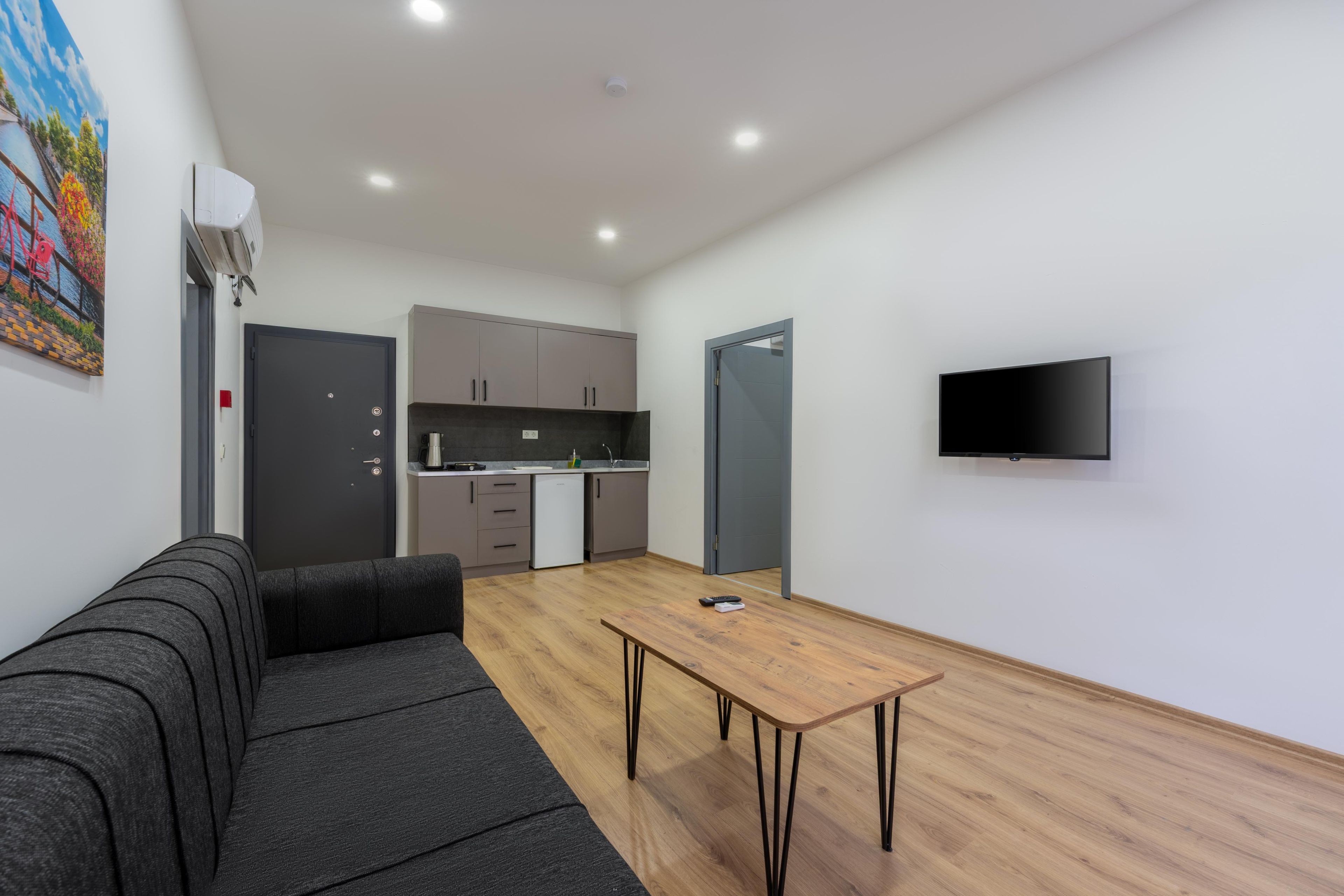 A modern living space with a sofa, a wooden table, a kitchen area, and a television mounted on the wall.
