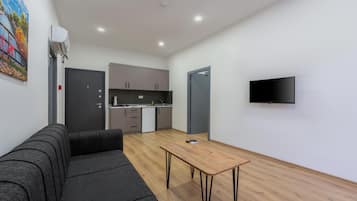 A modern living space with a sofa, a wooden table, a kitchen area, and a television mounted on the wall.