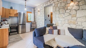 Eine kleine Küche mit Herd, Backofen und Kühlschrank, einer Steinsäule und einem blauen Sofa mit Kissen.