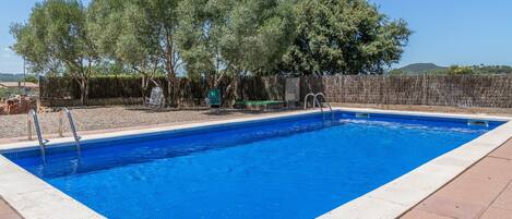 A rectangular swimming pool with clear blue water, surrounded by a tiled deck and a wooden fence.