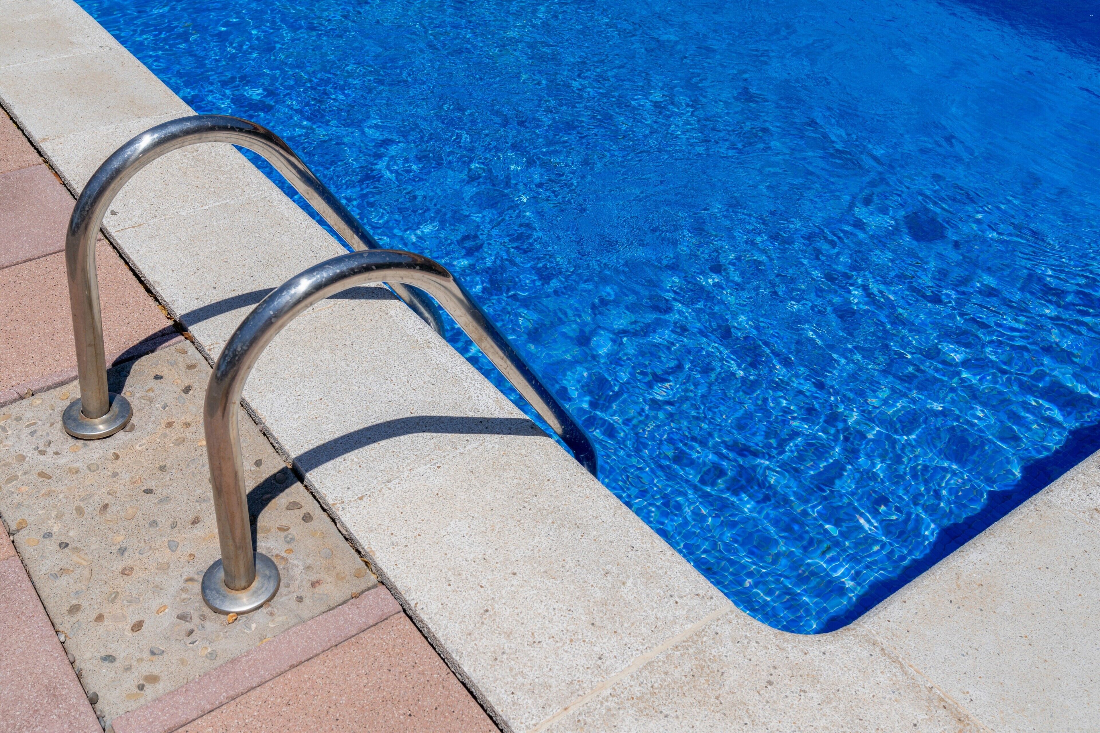 A swimming pool with clear blue water, a metal ladder, and a tiled deck.