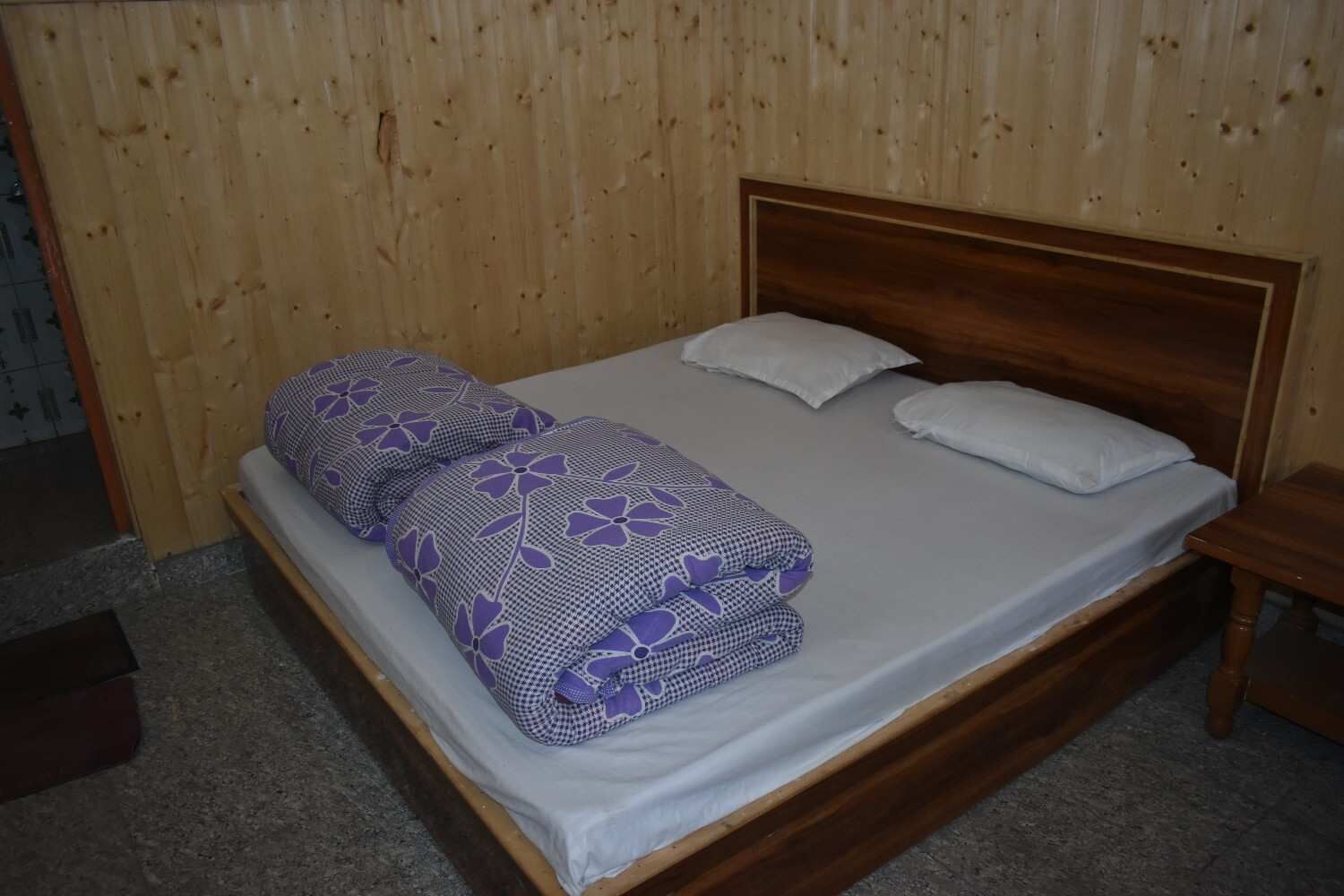A single bed with a wooden headboard, two pillows, and a blanket with a floral pattern.