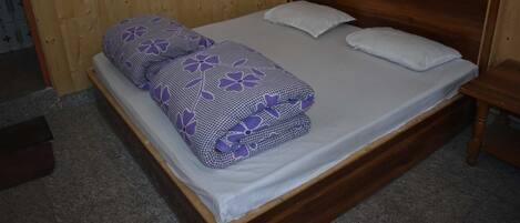 A single bed with a wooden headboard, two pillows, and a blanket with a floral pattern.