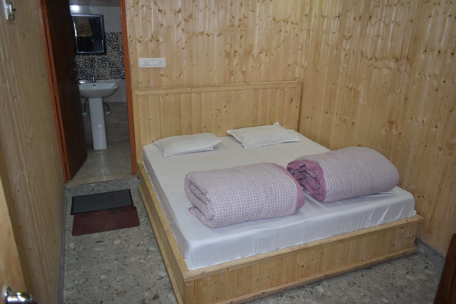 A wooden-paneled room with a bed, a sink, and a mirror.