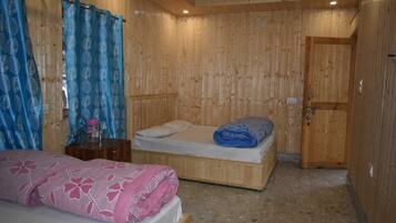 Una habitación con paneles de madera, dos camas, una puerta de madera y una pequeña mesa con una manta de diseño rosa y azul.
