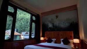 A bedroom with a wooden bed, two bedside lamps, a large window, and a forest mural on the wall. - Narayan Guest House Kasol (Kasol)