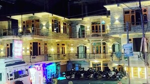 A multi-story building with illuminated windows and balconies, a parked motorcycle, and a vehicle labeled 'MEDICINE' in the foreground. - Narayan Guest House Kasol (Kasol)