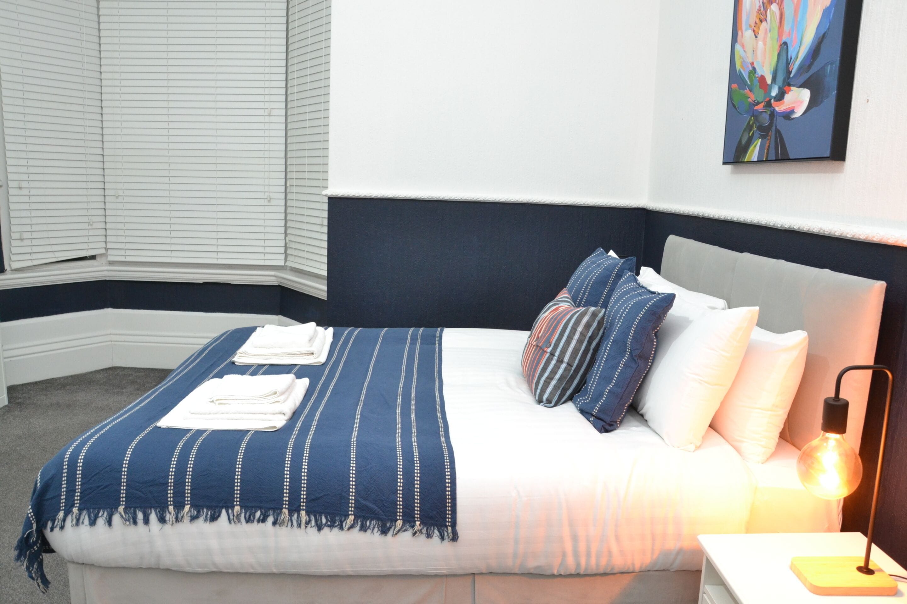 A neatly made bed with a striped blanket, pillows, and a bedside lamp.