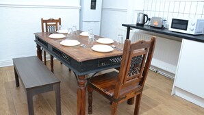 A dining area with a wooden table set for four, a bench, and a kitchen with a microwave and kettle.