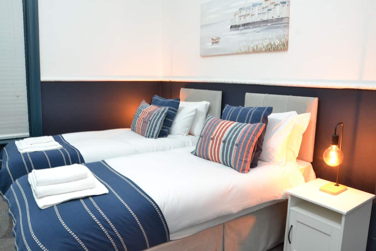 Habitación de hotel con dos camas, una mesita de noche con lámpara y un cuadro en la pared.