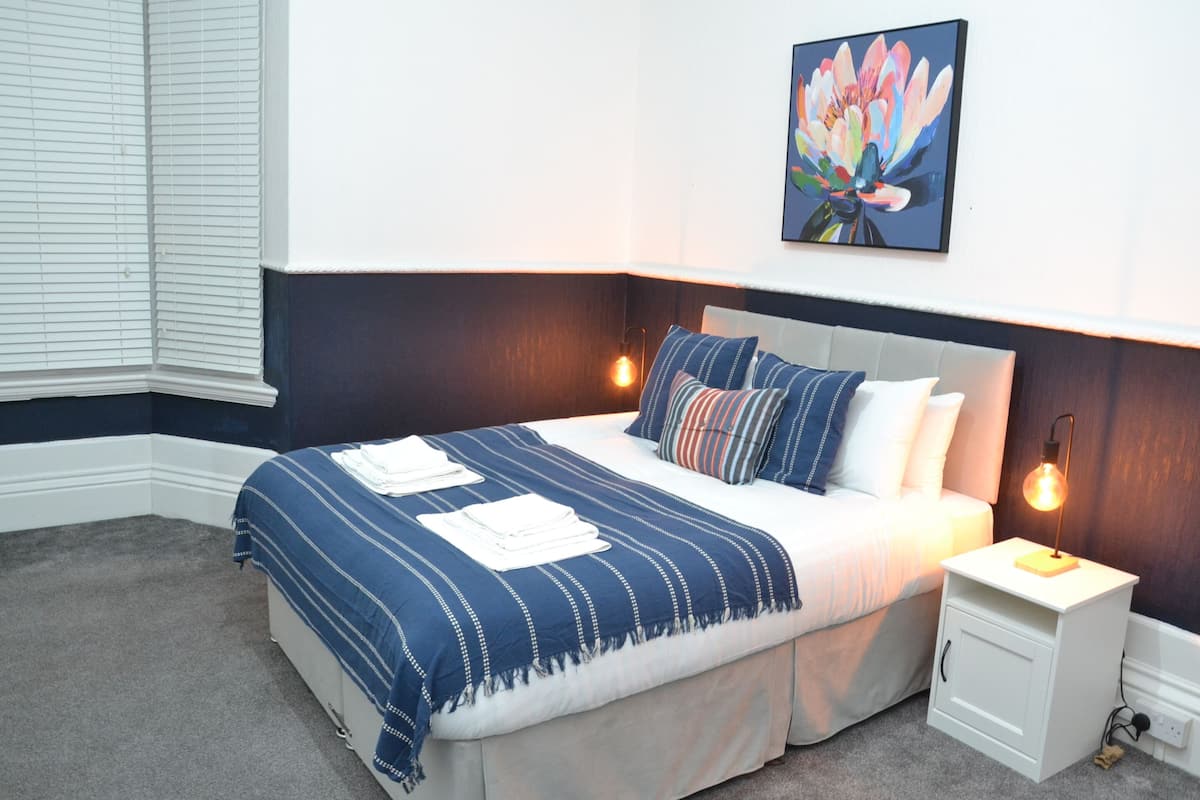Un dormitorio ordenado con cama, mesitas de noche y una obra de arte colgada en la pared.