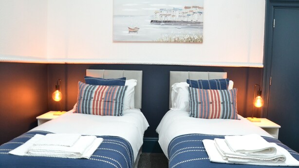 A hotel room with two beds, a painting of a coastal scene, and bedside lamps.
