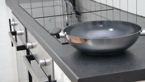 A kitchen with a black stovetop, a single pan, and a stainless steel range hood.