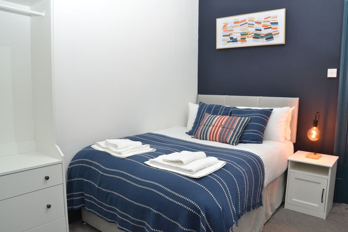 Una cama bien hecha con un edredón a rayas, una lámpara de noche y una obra de arte en la pared.
