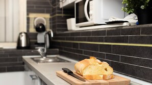 A kitchen with a loaf of bread on a cutting board, a knife, a kettle, and a microwave on the counter. - Cozy 45m2 apartment, ideal for 4 people, located on the ground floor of a building.The accommodation is located in a residential area 2 steps from the famous Prada Foundation, center of culture and fashion, and a short distance from the Milano Porta Rom (Milan)