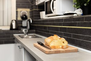 A kitchen with a loaf of bread on a cutting board, a knife, a kettle, and a microwave on the counter. - Cozy 45m2 apartment, ideal for 4 people, located on the ground floor of a building.The accommodation is located in a residential area 2 steps from the famous Prada Foundation, center of culture and fashion, and a short distance from the Milano Porta Rom (Milan)