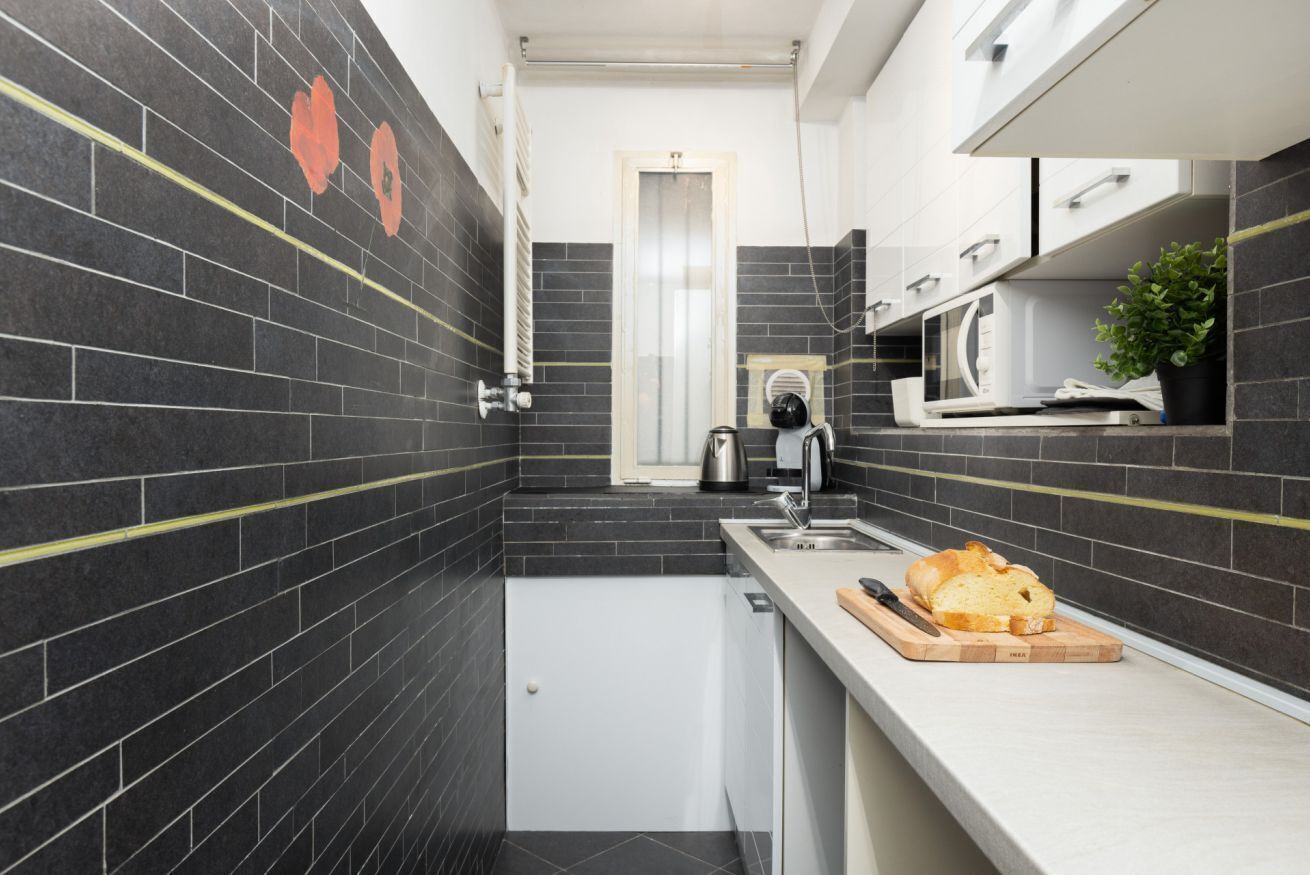 Eine moderne Küche mit schwarzen Fliesen, einer weißen Arbeitsplatte, einem Spülbecken, einem Wasserkocher und einem Brot auf einem Schneidebrett.